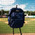  A navy Tater Baseball bat bag backpack hanging from the netting of a professional baseball field. The spacious and stylish bag is designed to carry all your essential gear and is made for players who demand the best.