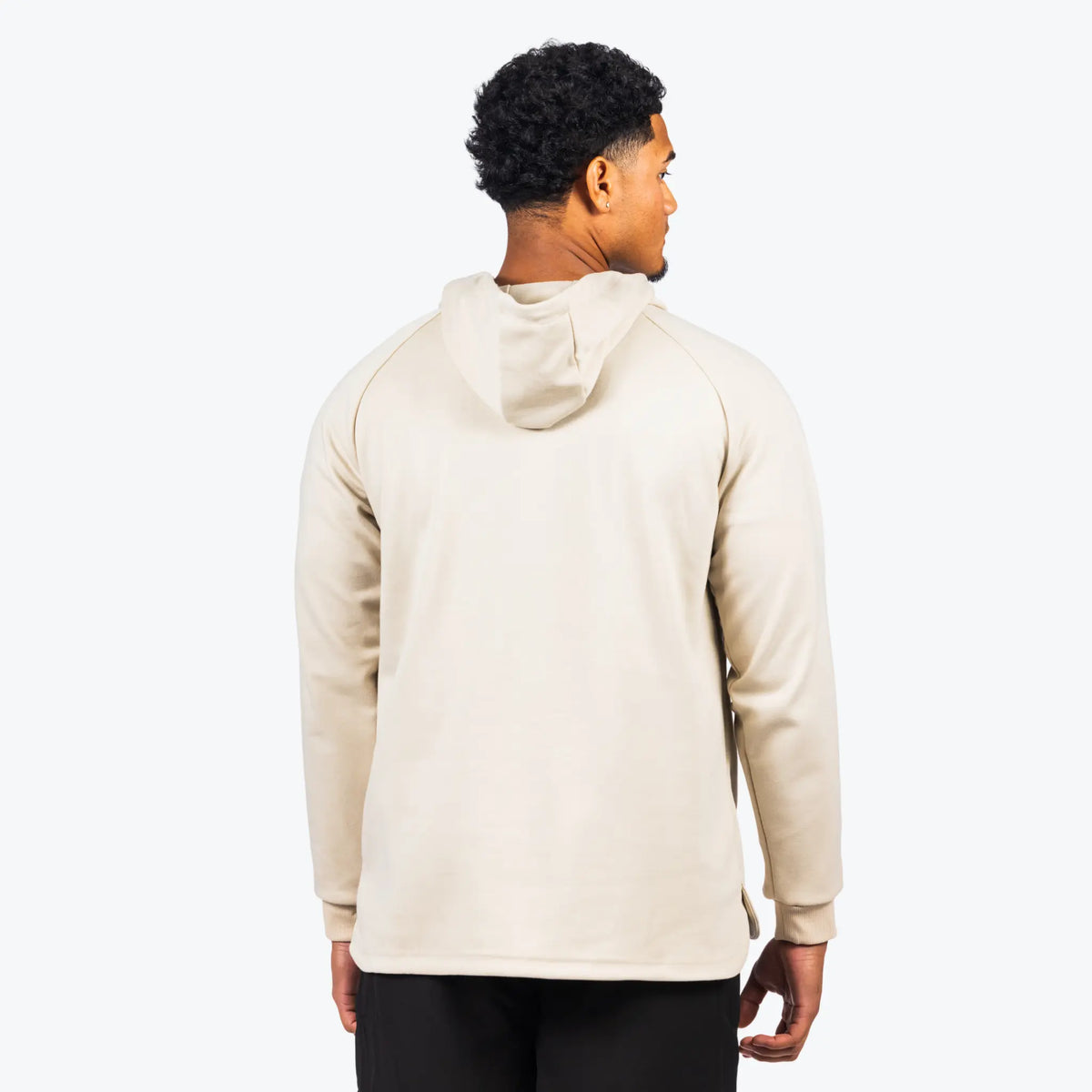 The image shows the backside view of a person wearing a cream-colored athletic hoodie. The hoodie has long sleeves and is part of a training or athleisure outfit. The individual appears to be looking to the side, and the hoodie seems to have a relaxed and comfortable fit, which is typical for workout or casual wear.