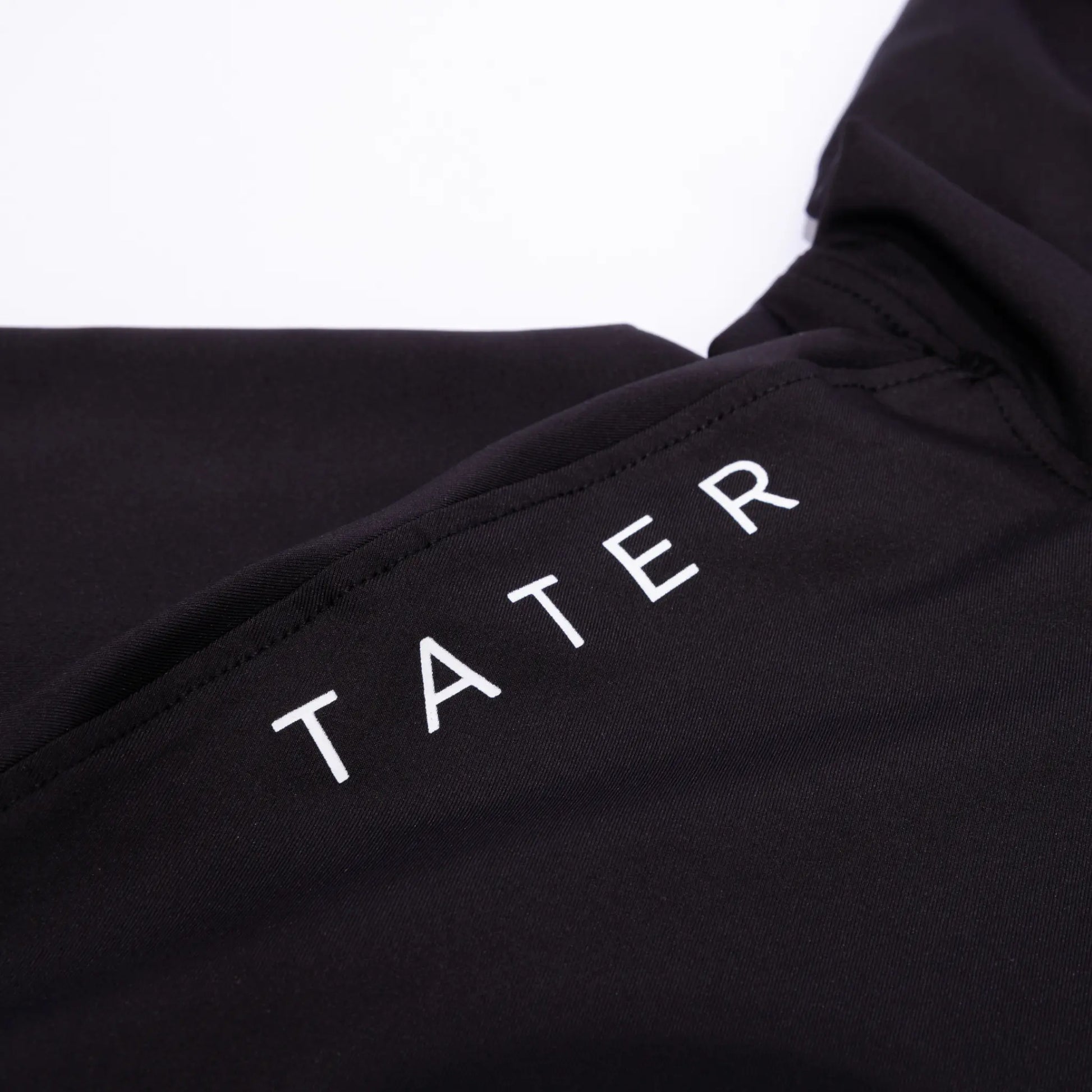 "Detail of a black short-sleeve baseball hoodie with the 'TATER' logo printed in white, part of the Tater Baseball FUNDAMENTALS collection.
