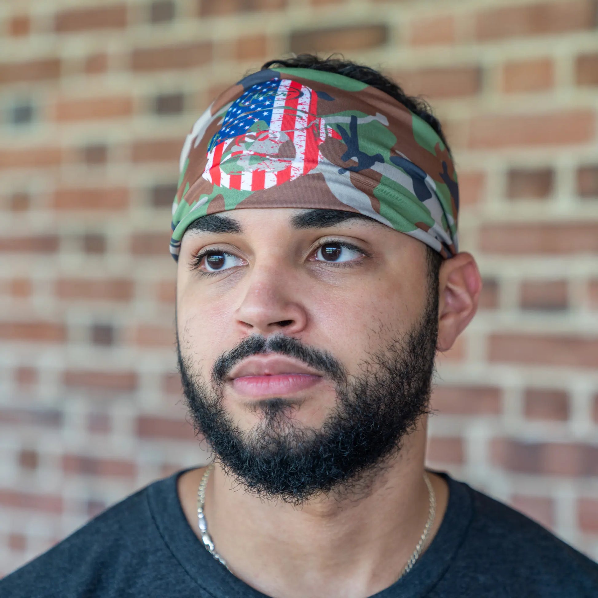 Focused baseball player wearing Tater Baseball's camo workout headband adorned with the American flag, blending athletic function with national pride in a casual setting.