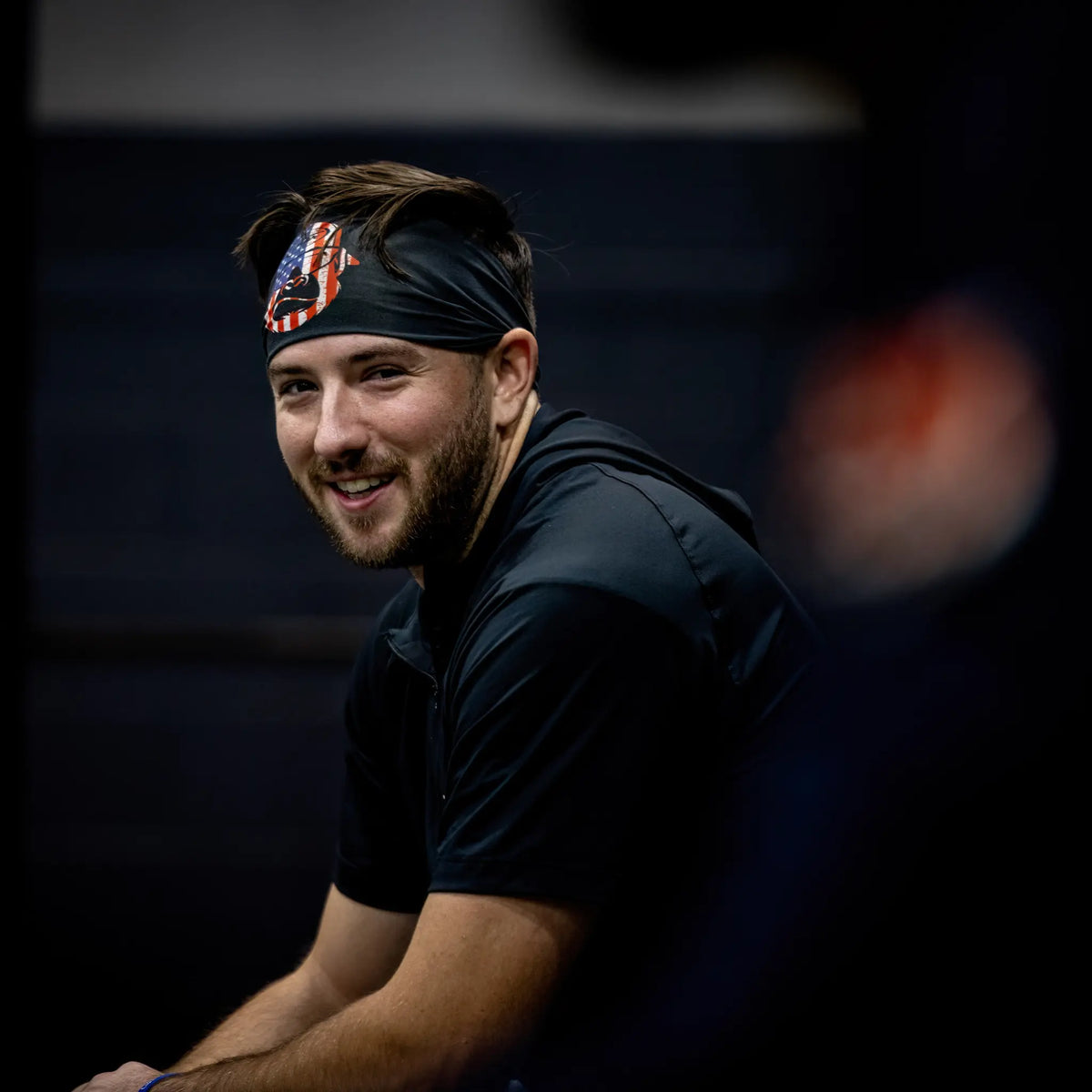 Smiling athlete wearing Tater Baseball&#39;s black headband with a bold USA flag Kong design, providing both performance and patriotic style during training.